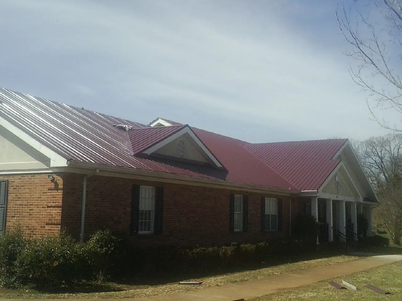 Red metal roof with gabled entries on a long brick building, from a Hail Damage Roof Repair job in Campti