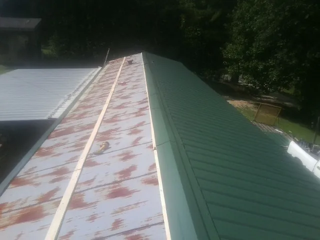 Old rusted panels beside newly installed green metal roofing — Wind Damage Roof Repair by Roofing Brothers in Campti