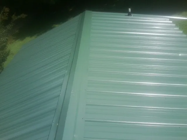 New green metal panels meeting at the ridge of a roof — Flat Roof Repair work by our crew in Campti