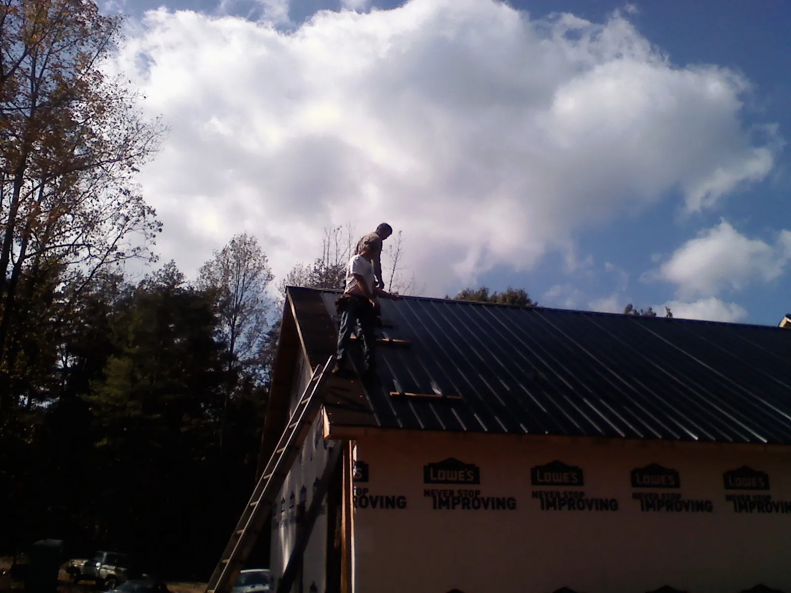 Roofer fastening dark metal panels high against a cloudy sky, from a Roof Inspection job in Campti