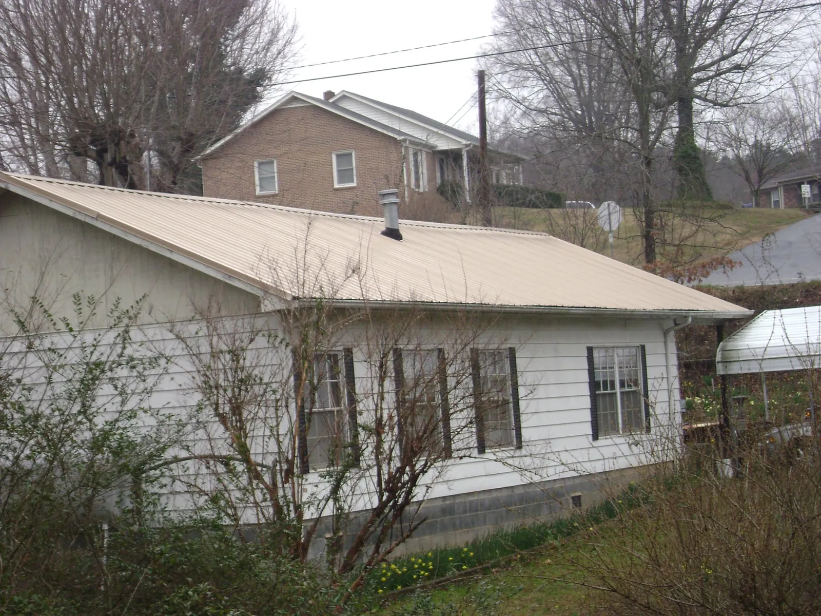 Tan metal roof on a white sided house set into a hillside — Commercial Roofing by Roofing Brothers in Campti