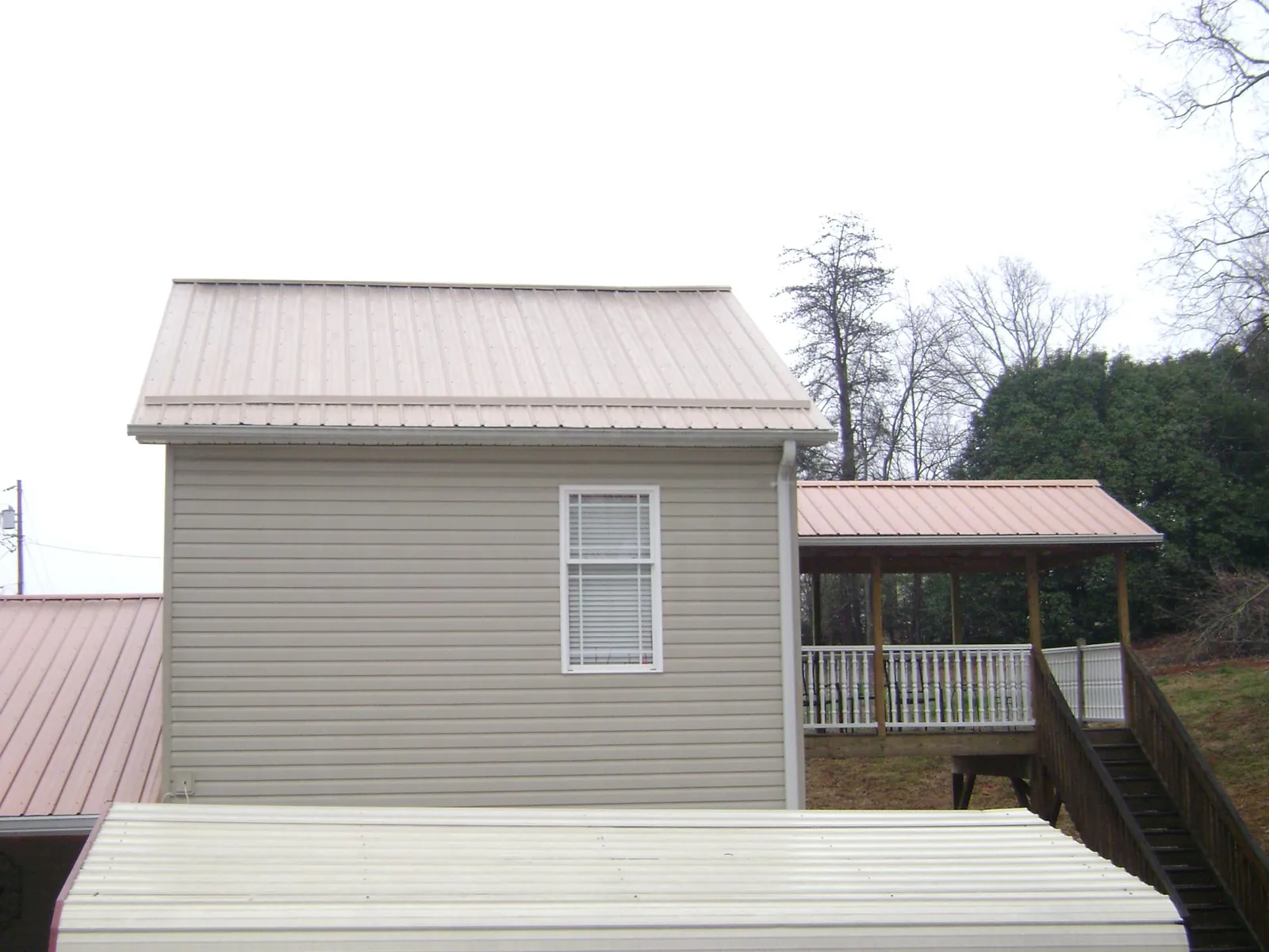 Tan metal roofs on a two story addition and attached porch, from a Roof Replacement job in Campti